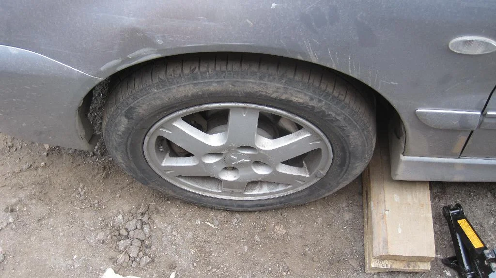 Передние колесо Mitsubishi Lancer IX затянуто. Автомобиль опущен с домкрата. Домкрат и доски лежат рядом с автомобилем.