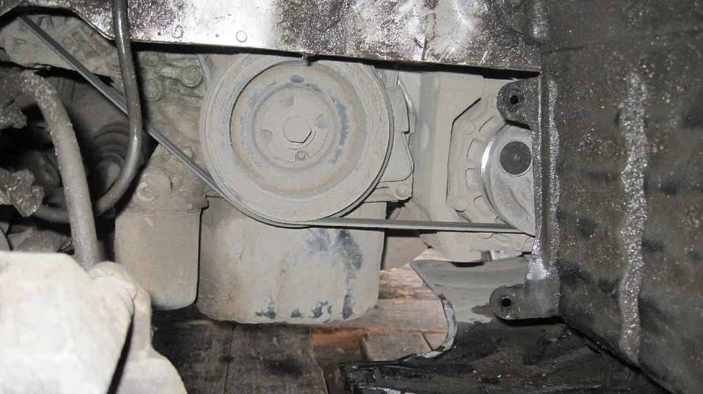 Пластиковая защита справа от двигателя Mitsubishi Lancer IX снята. Видно крив коленчатого вала с приводными ремнями.