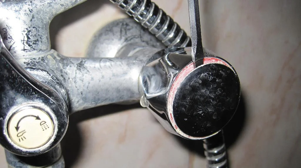 Смеситель для ванны IDDIS установлен, снятие заглушки ручки крана отверткой.