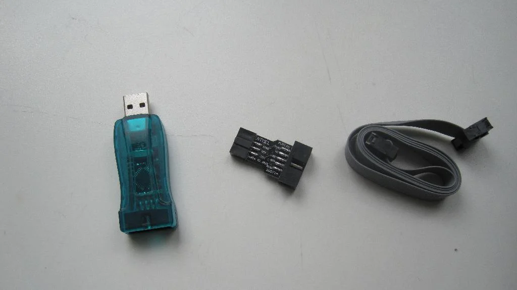 USBasp, кабель подключения, переходник с 10pin на 6pin лежат на белом столе.