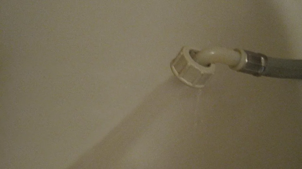 Вода льется из заливного шланг стиральной машины в ванну белого цвета.