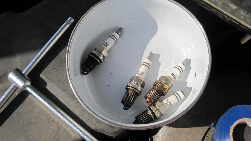 Свечи зажигания для двигателя TU3JP лежат в миске, рядом с миской лежит свечной ключ