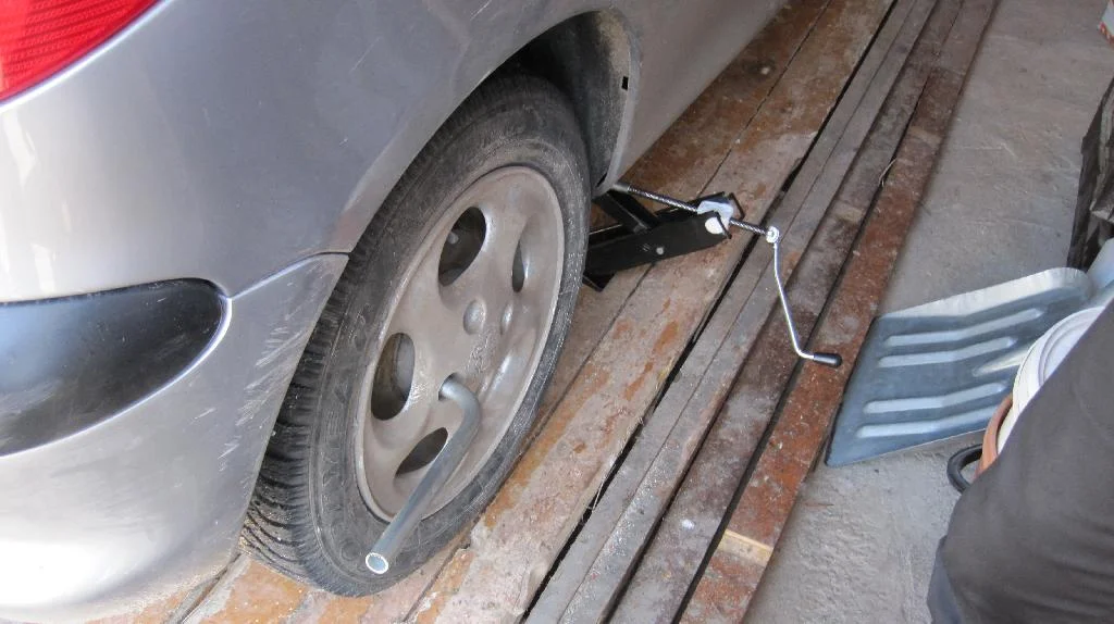 Ослабляем гайки заднего колеса ключом, установка домкрата под автомобиль Peugeot 206