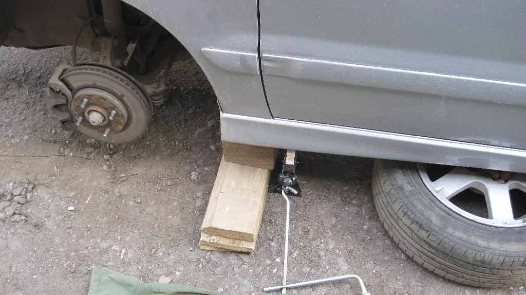 Автомобиль Mitsubishi Lancer IX стоит на досках со снятым передним колесом, которое лежит под автомобилем