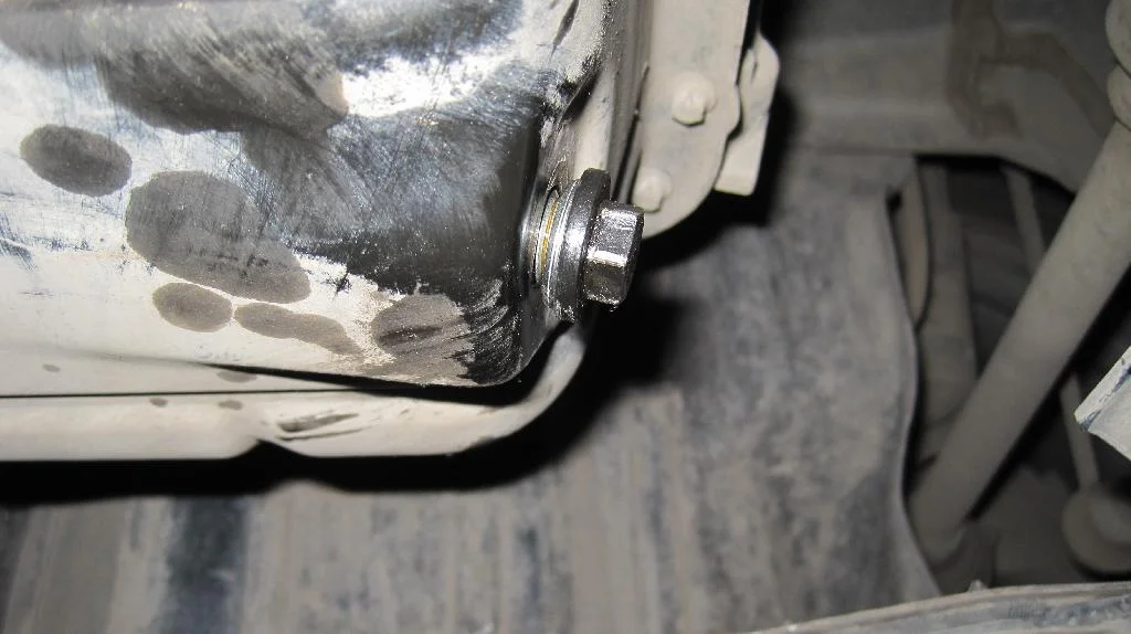 Сливная пробка с новой прокладкой закручена не до конца в поддон двигателя Mitsubishi Lancer X. Видно не сжатую новую прокладку сливной пробки масляного поддона двигателя.