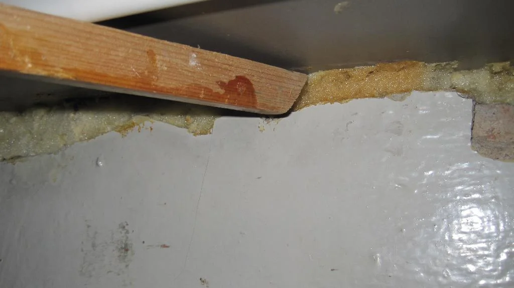 Срезанная монтажная пена заталкивается бруском на стыке подоконника и стены.